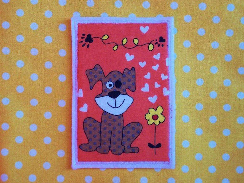 May include: A rectangular patch with a cartoon dog design. The dog has brown spots, a large smile, and one black eye. The patch is set against an orange background with white hearts and a yellow flower, and has a white border.