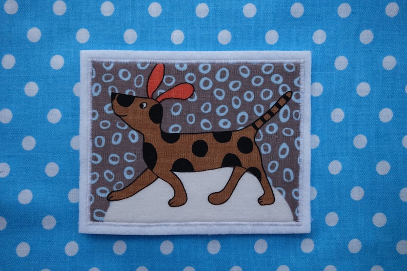 May include: A brown and black spotted dog with orange ears is walking on a white background with a grey and blue polka dot pattern. The dog is looking to the left.