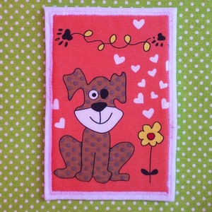 May include: A rectangular patch with a cartoon dog design. The dog is brown with spots, a white face, and a black nose, set against a red background. White hearts and a yellow flower are also present. The patch has a white border, on a green polka dot background.