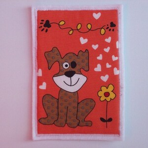May include: An orange fabric patch featuring a cartoon dog illustration. The dog is brown with darker brown spots, a white face, and a black nose. White hearts and a yellow flower are also featured. The patch has a white frayed edge.