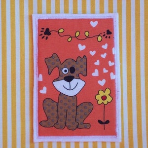 May include: An orange rectangular patch with a cartoon dog illustration. The dog has brown spots, a smiling face, and a single eye. White hearts and a yellow flower are also present. The patch is bordered with white and set against a yellow and white striped background.