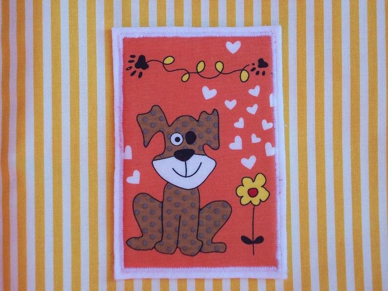 May include: An orange rectangular patch with a cartoon dog illustration. The dog has brown spots, a smiling face, and a single eye. White hearts and a yellow flower are also present. The patch is bordered with white and set against a yellow and white striped background.