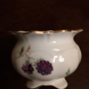 May include: White porcelain sugar bowl with a scalloped rim and gold trim. The bowl features a floral design with purple flowers and green leaves.