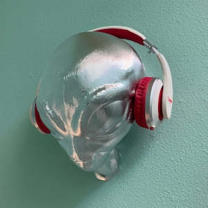 Puede incluir: Una escultura de cabeza de alienígena plateada con auriculares rojos y blancos.