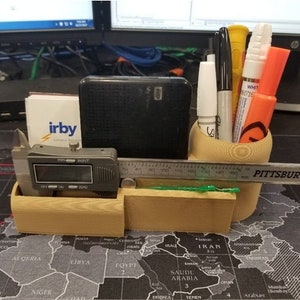 May include: A wooden desk organizer with a ruler, a black and silver caliper, and a variety of pens and markers. The organizer has a compartment for each item. The organizer is sitting on a desk with a world map.