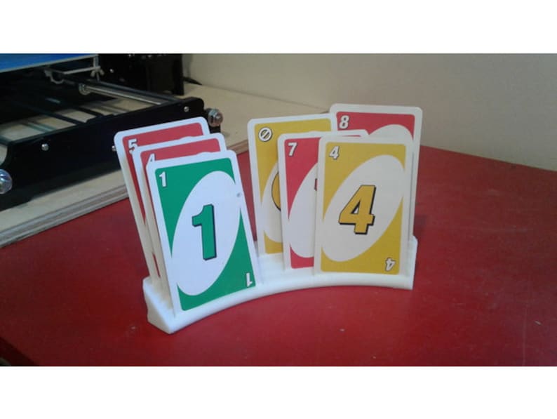 May include: A white plastic card holder with a curved design holds a stack of UNO cards. The cards are red, yellow, green, and blue with numbers and symbols.