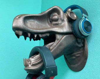 May include: A bronze dinosaur head sculpture with a blue and silver headphone hanging from its mouth. The dinosaur head is mounted on a wall.