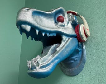 May include: A blue and silver dinosaur head sculpture with red headphones. The dinosaur's mouth is open and its eyes are red.