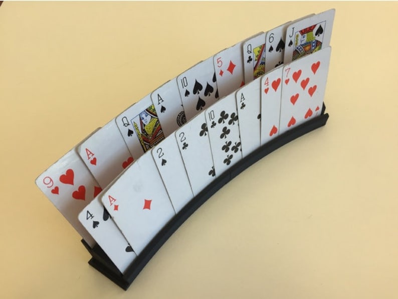 May include: A black plastic card holder with a curved design holds a deck of playing cards. The cards are fanned out, showing the face of each card. The cards include Ace, Queen, Jack, 10, 9, 7, 6, 5, 4, 2, and Ace.