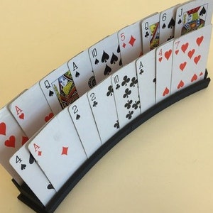 May include: A black card holder with a curved design holds a deck of playing cards fanned out. The cards are arranged in order from 9 of hearts to Jack of spades.