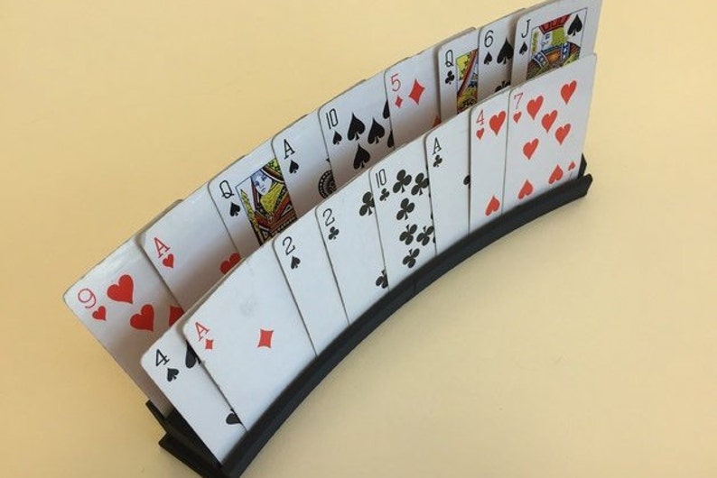 May include: A black card holder with a curved design holds a deck of playing cards fanned out. The cards are arranged in order from 9 of hearts to Jack of spades.