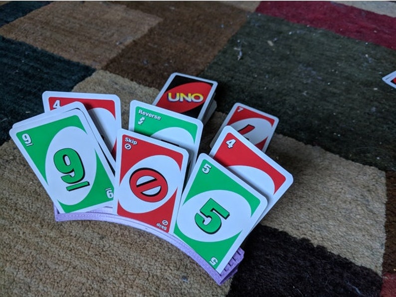 May include: A purple card holder with a stack of UNO cards, including a green card with the number 9, a red card with the word "Skip", a green card with the number 5, and a red card with the number 4.