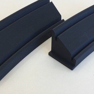 May include: Two black plastic track pieces for a toy race car set. The pieces are curved and have a raised edge.