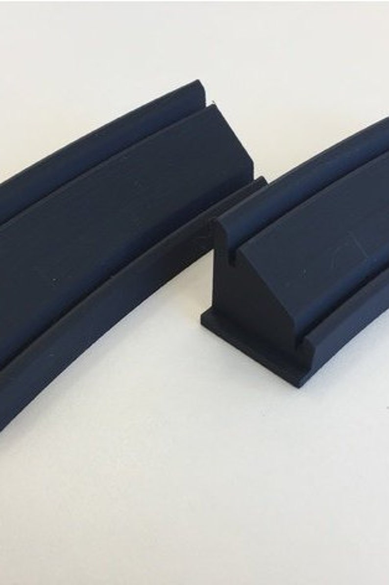 May include: Two black plastic track pieces for a toy race car set. The pieces are curved and have a raised edge.