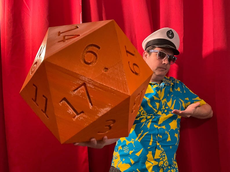 Pu&ograve; includere: Grande dado D20 arancione con numeri bianchi. Il dado &egrave; tenuto da una persona che indossa un cappello da capitano, occhiali da sole e una camicia floreale blu e gialla. Lo sfondo &egrave; una tenda rossa.