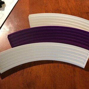 May include: Three curved pieces of plastic track, one white, one purple, and one white. The track pieces are designed to connect together to form a curved track.