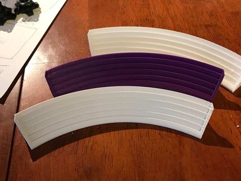 May include: Three curved pieces of plastic track, one white, one purple, and one white. The track pieces are designed to connect together to form a curved track.