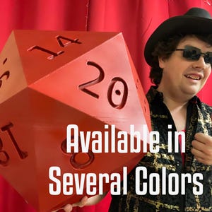 Pu&ograve; includere: Grande dado rosso a venti facce con numeri bianchi. Il testo "Available in Several Colors" &egrave; visualizzato sull'immagine. Il dado &egrave; tenuto da una persona con cappello nero e occhiali da sole.