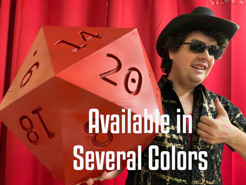Pu&ograve; includere: Grande dado rosso a venti facce con numeri bianchi. Il testo "Available in Several Colors" &egrave; visualizzato sull'immagine. Il dado &egrave; tenuto da una persona con cappello nero e occhiali da sole.