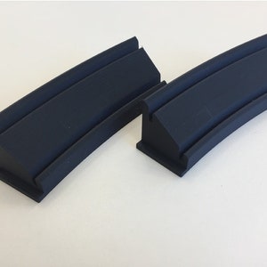 May include: Two black rubber track pieces for a model train set. The pieces are curved and have a raised lip on the inside.