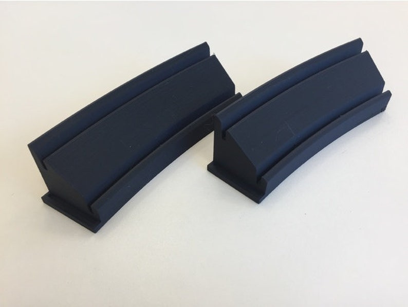 May include: Two black rubber track pieces for a model train set. The pieces are curved and have a raised lip on the inside.