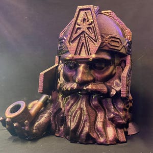 May include: A 3D-printed bust of a dwarf with a long beard, helmet, and pipe. The sculpture is primarily bronze with purple and gold highlights. The dwarf is holding a pipe in his right hand.