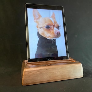 Puede incluir: Un soporte de madera marrón con una tableta que muestra una foto de un chihuahua con gafas redondas. El chihuahua lleva un jersey de cuello alto negro.