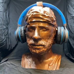 Könnte beinhalten: Eine bronzene Büste einer Person, die blaue Kopfhörer trägt. Die Kopfhörer sitzen auf dem Kopf und die Ohrmuscheln bedecken die Ohren.
