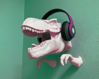 May include: A pink dinosaur head sculpture with a purple and black pair of headphones on its head. The dinosaur is mounted on a wall.