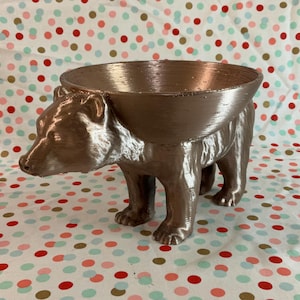 Może przedstawiać: Misa w kształcie niedźwiedzia w kolorze miedzianym z okrągłym, pustym wierzchołkiem. Misa wykonana jest z gładkiego, błyszczącego materiału i ma realistyczny wzór niedźwiedzia.
