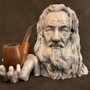 May include: A 3D printed bust of a man with a long beard and a pipe in his hand. The bust is gray and the pipe is brown.