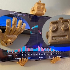 May include: Gold-colored robot head and hands attached to a TV screen displaying a stock chart. The robot head is square with circular eyes and a rectangular mouth. The hands are open, as if holding the screen.