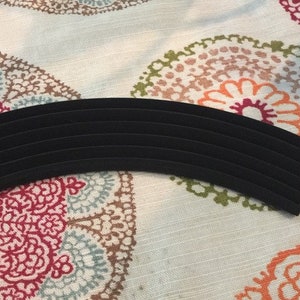 May include: A black velvet ring holder with multiple slots for storing rings. The holder is curved and has a smooth, soft surface.