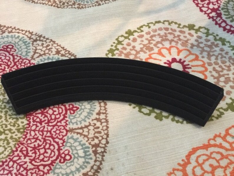 May include: A black velvet ring holder with multiple slots for storing rings. The holder is curved and has a smooth, soft surface.