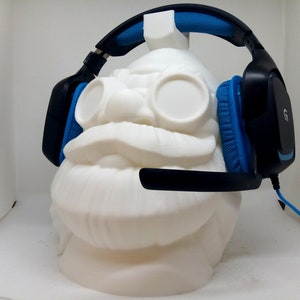 May include: Black and blue gaming headset with a microphone, resting on a white 3D printed bust.