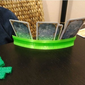 May include: A green card holder with four cards inside. The cards are white with blue and gold designs. The holder is curved and has a smooth surface.