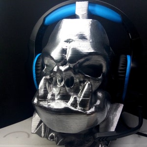 May include: A silver 3D printed skull with a headset resting on it. The headset has black earcups with blue accents.