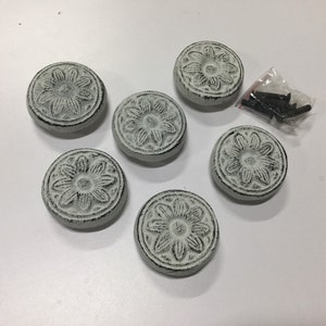 May include: Six white cast iron drawer pulls with a floral design. The pulls are round and have a distressed finish. The pulls come with screws.