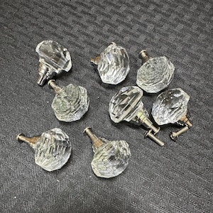 May include: Eight clear glass crystal cabinet knobs with silver metal hardware. The knobs are faceted and have a diamond-like shape.