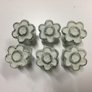 May include: Six white cast iron drawer pulls with a distressed finish. Each pull is shaped like a flower with a circular center.