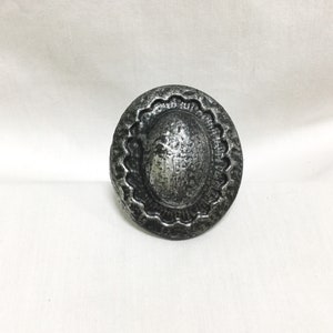 May include: A silver metal decorative knob with a raised, oval center and a scalloped edge.