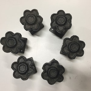 May include: Six black cast iron flower-shaped drawer pulls with a square base.