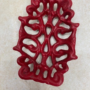 May include: A red cast iron soap dish with a decorative, intricate design. The dish is shaped like a leaf with a raised, floral pattern.