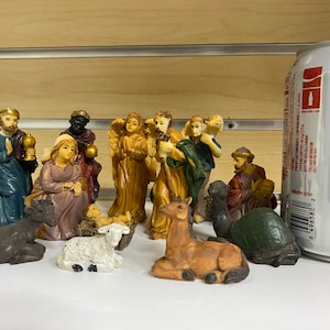 Op de afbeelding: Een kerststalfigurenset met verschillende figuren, waaronder Maria, Jozef, baby Jezus, een ezel, een schaap, een kameel en drie wijzen. De figuren zijn gemaakt van geverfd hars en zijn ongeveer 10 cm hoog.