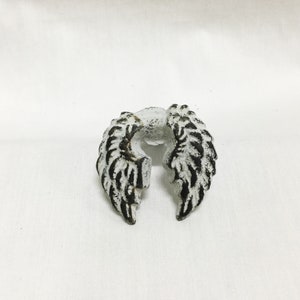 May include: White metal angel wing drawer pull with black detailing.