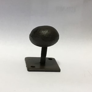 May include: A black metal hook with a round ball top and a square base. The hook is attached to a wall with screws.