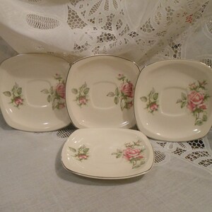 May include: Set of four white ceramic saucers with a gold rim and a floral design featuring pink roses and green leaves.