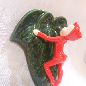 May include: A ceramic wall planter shaped like a green leaf with a red elf figurine climbing up the side.