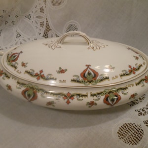 May include: An oval white serving dish with a lid. The dish has a gold trim and a floral design in shades of red, green, and black.