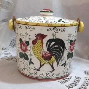 May include: A ceramic rooster cookie jar with a lid. The jar is white with a rooster illustration, red roses, and green vines. The lid has a red and green knob and yellow handles. The jar is approximately 7 inches tall.